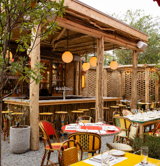 Outdoor restaurant patio with wooden pergola, bistro tables and colorful woven chairs, and ambient globe lighting
