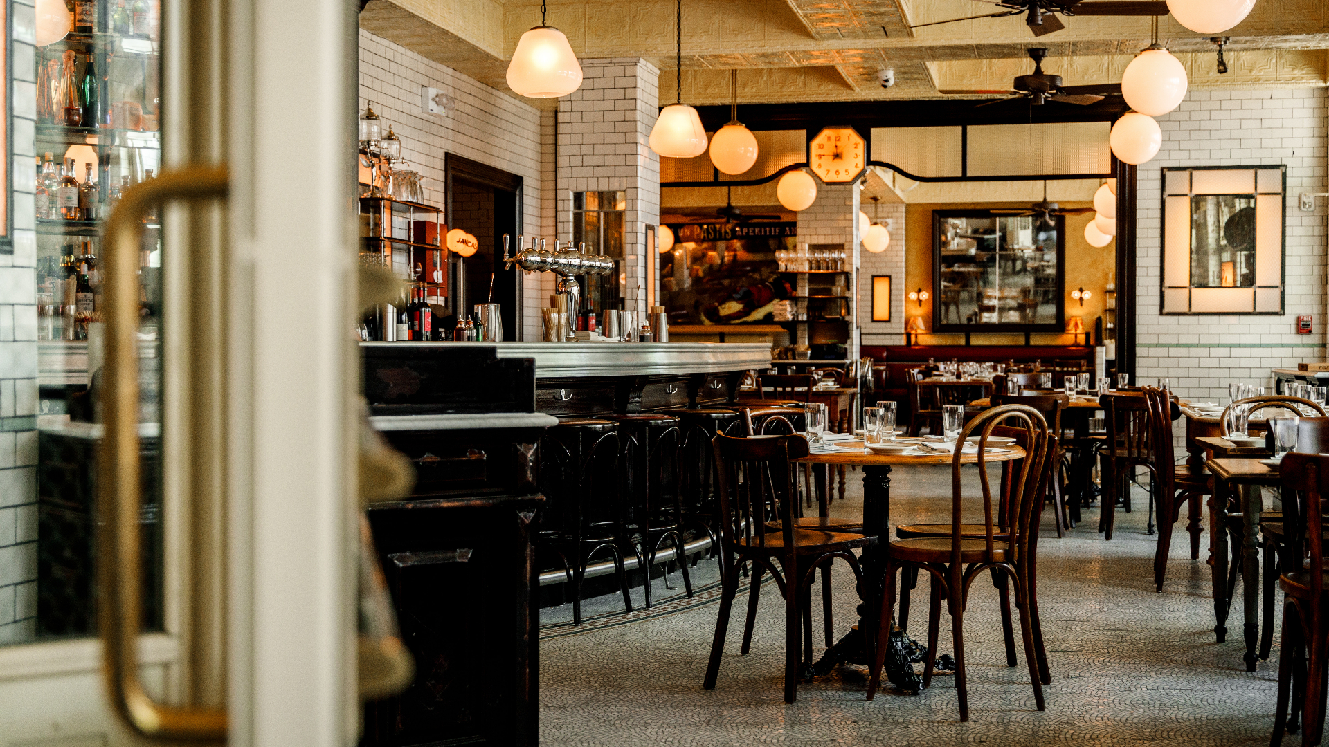 Modern restaurant interior with white subway tile walls, globe pendant lights, dark wood chairs, and bar seating area