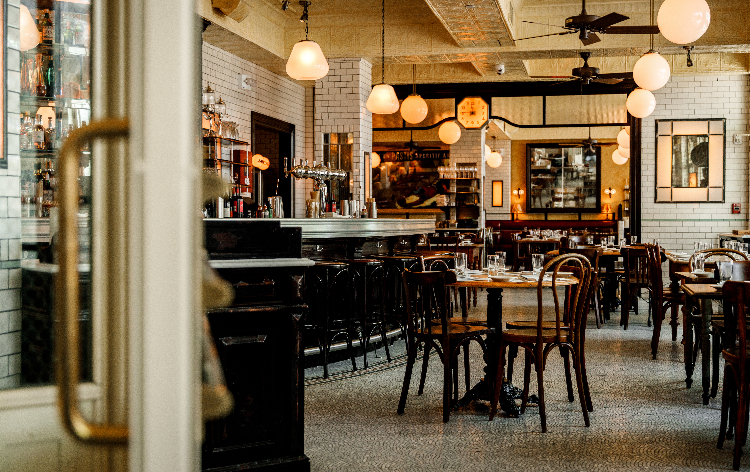 Modern restaurant interior with white subway tile walls, globe pendant lights, dark wood chairs, and bar seating area
