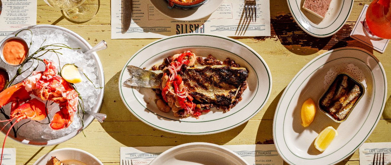 Overhead view of seafood dishes including lobster on ice, grilled fish with lobster tail, and sardines with lemon wedges